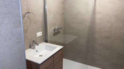 Moderne badkamer met witte spoelbak, donkere badmeubel en glazen douchecabine