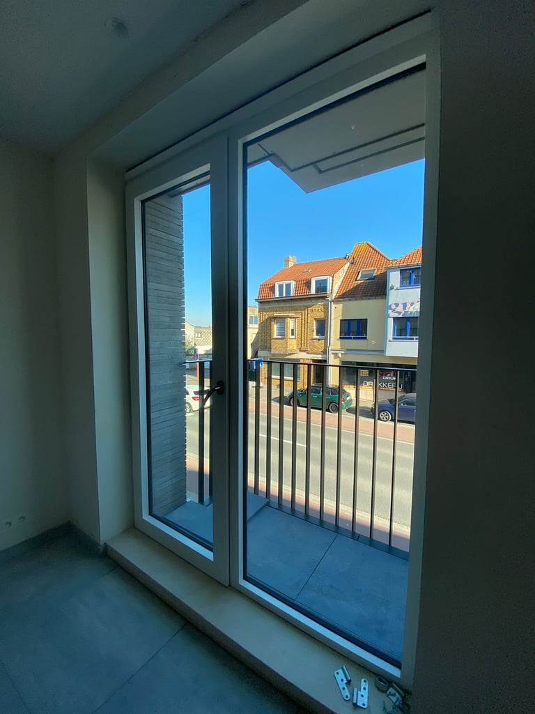 Uitzicht door dubbele glazen deuren met hekwerken naar Europese gebouwen met terracotta daken en heldere blauwe hemel