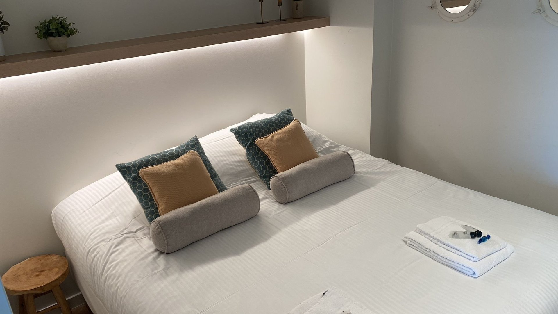 Moderne slaapkamer met wit bed, grijs gestoffeerd hoofdbord met sfeerverlichting en decoratieve kussens