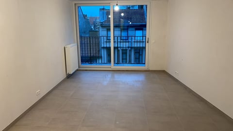 Empty apartment interior with gray tile flooring and glass balcony doors